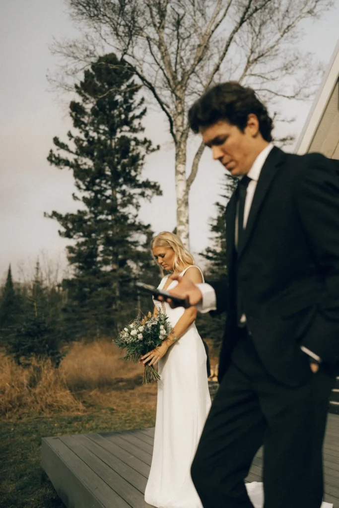 Bride holding bouquet while groom walks ahead outdoors