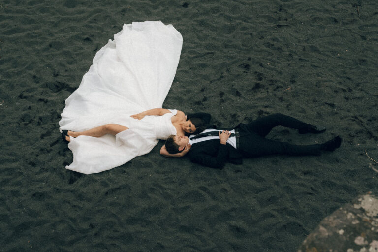 intimate north shore wedding couple laying on black beach sand